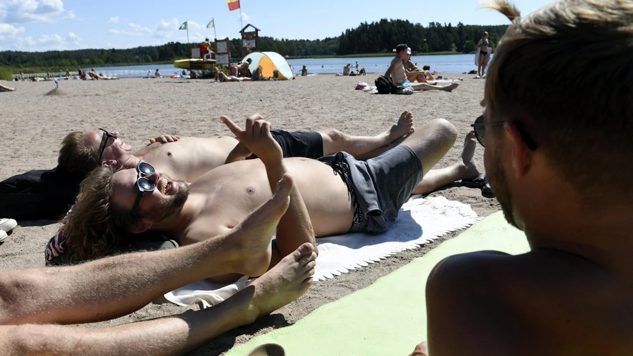 Turkulainen Mikko Helle (kesk.) ottaa aurinkoa ystäviensä kanssa Ekvallan uimarannallla Kakskerrassa Turussa 24. heinäkuuta 2019. LEHTIKUVA / MARTTI KAINULAINEN