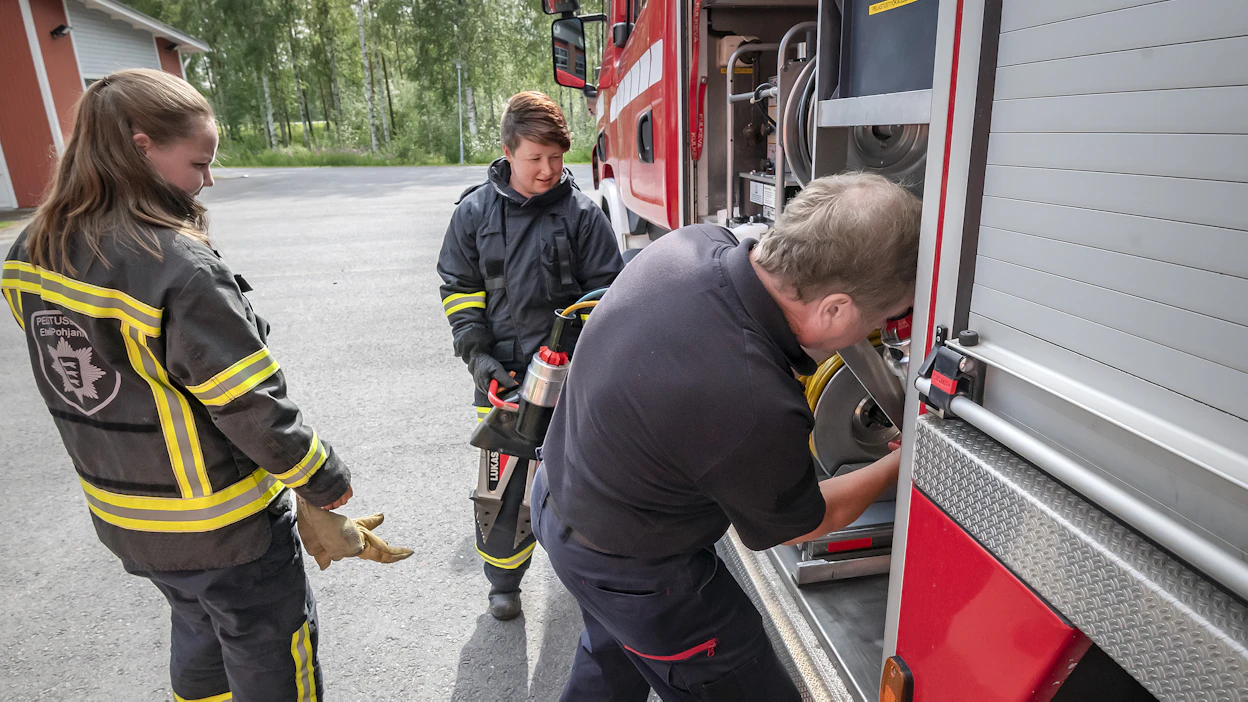 Sopimuspalokunnan tytöt, Iida Mäntylä sekä Karoliina Sulkakoski ja palomies Jari Övermark pakkasivat raivauskalustoa Evijärven palokunnan autoon vuonna 2018.