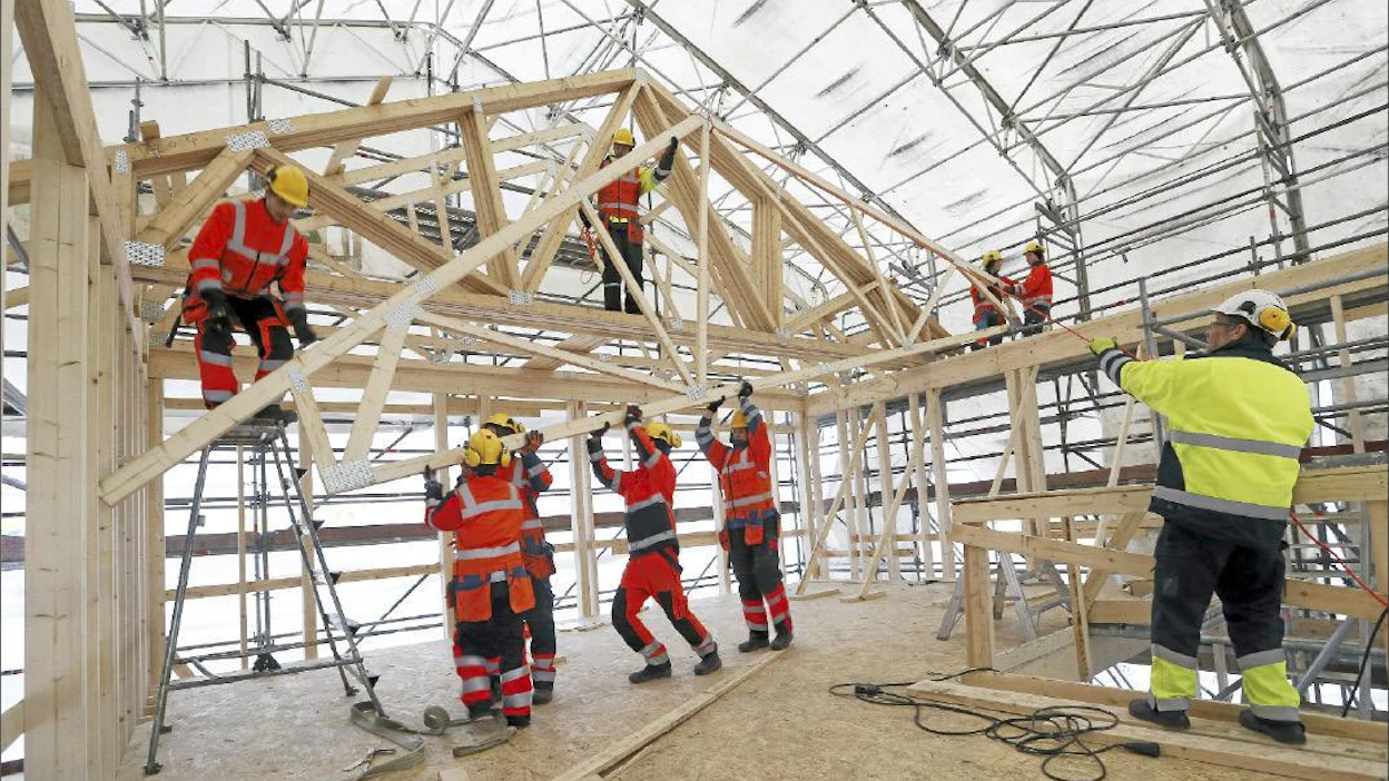 Oulun seudun ammattiopiston talonrakennusopiskelijat rakentavat oppilastyönä kolme omakotitaloa Oulun Hiukkavaaran uudelle asuinalueelle. Opettaja Erkki Valkonen keltaisessa työtakissa johtaa kattotuolien nosto-operaatiota. Pekka Fali