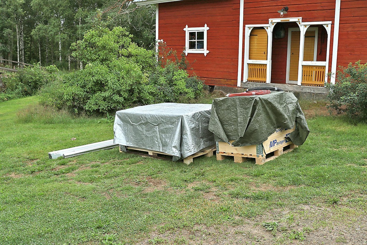 Tarvittavat komponentit saapuivat paikalle muutama päivä ennen asentajaa. Hopeisen kevytpeitteen alla ovat paneelit, vihreän peitteen alla kiinnikkeet, invertteri ja muut oheistarpeet. Myös alumiinkiskot kuuluvat tarvikkeisiin.