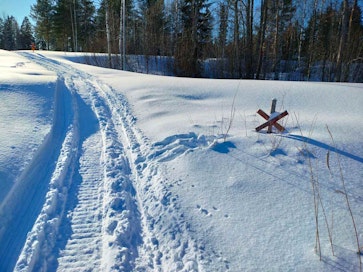Moottorikelkan jälki hangella ja vieressä kelkkareitin risteyksen merkki.