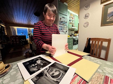 Nainen järjestelee vanhoja valokuvia käsissään. Irja Jefremoff. 