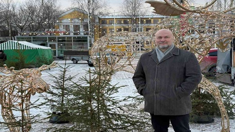 Mies seisoo jouluisella torilla joulukuusien ja jouluvalojen keskellä.