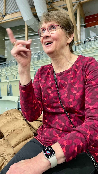 Nainen osoittaa sormella ylöspäin. Arja Pappinen istuu Joensuun Areenassa. 