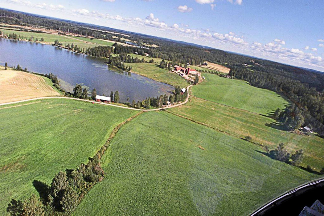 Ilmakuva: järvi,talouskeskus, peltoa, metsää. (Metsän lentolannoitus. Pilotti Ismo Matinlassi levittää neulasanalyysin perusteella valmistettua puuston terveyslannoitetta.)
ympäristö
