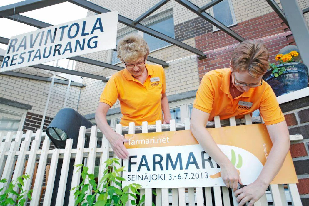 Farmari Trahteeri-ravintola.
Heli Kallio (oik.) ja Hannele Laurila kiinnittävät Farmari-mainoskylttiä ravintola Trahteerin terassilla.