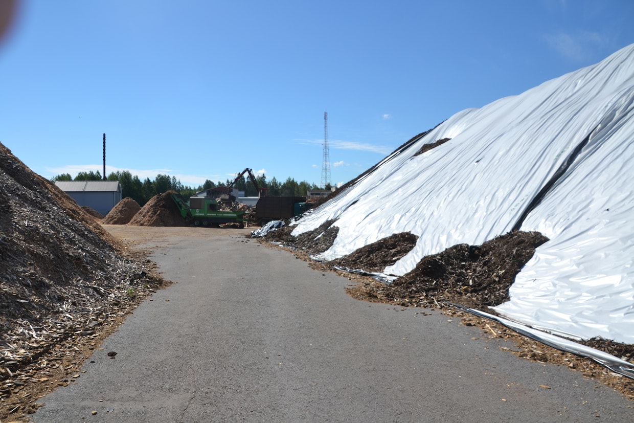 Terminaalissa on erilaisia poltettavia eriä. Kun haketus aloitetaan, niin sitä tehdään vähintään 1 000 m³ kerralla, jolloin hakkurikuskin ei tarvitse usein vierailla. Ylivuotinen turve on kuvassa oikealla muovin alla. Ainakin ne kasat peitetään, joita säilytetään pidempään. Kurottajan kanssa ulottuu 13 metriin, jolla saadaan rulla nostettua kasalle.