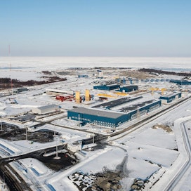 Pyhäjoen Hanhikivenniemellä on aidattu sadan hehtaarin kokoinen työmaa-alue ydinvoimalalle. Siniset rakennukset etualalla ovat raudottamoja ja keltaiset siilot betoniasemia. Hallintorakennus on työn alla, samoin louhinta voimalan perustuksia varten.
