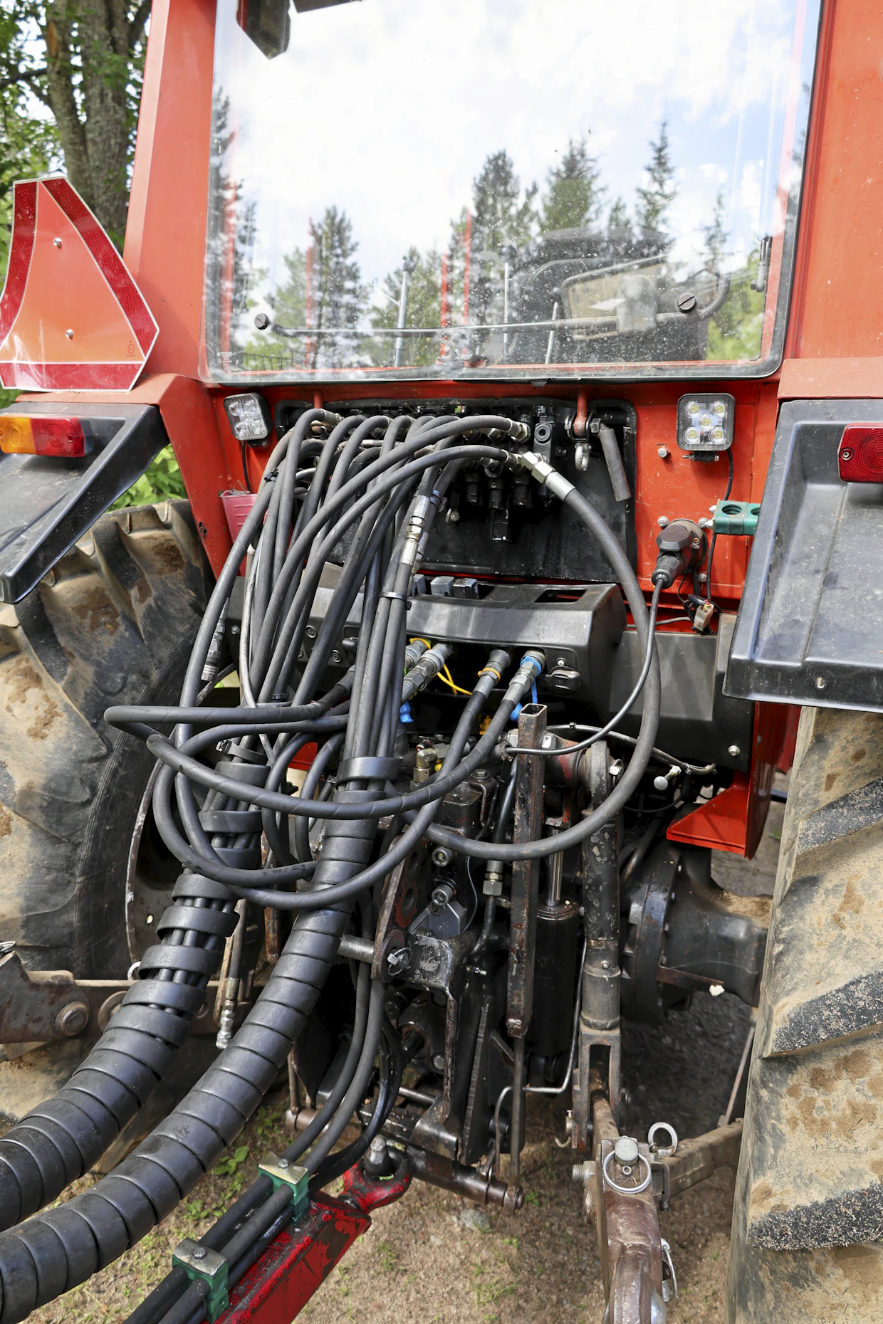 Projektin aloitustilanteessa traktorin takana näytti tältä. Lavavarusteisen metsäperävaunuyhdistelmän liittäminen vaati seitsemän pikaliittimen kytkemistä. Lisäksi letkut eivät kulkeneet ihanteellisia reittejä, vaan osuivat toisiinsa. Pieniä korjausyrityksiä oli tehty, esimerkiksi nosturiventtiilin letku oli vaihdettu lyhyempään.