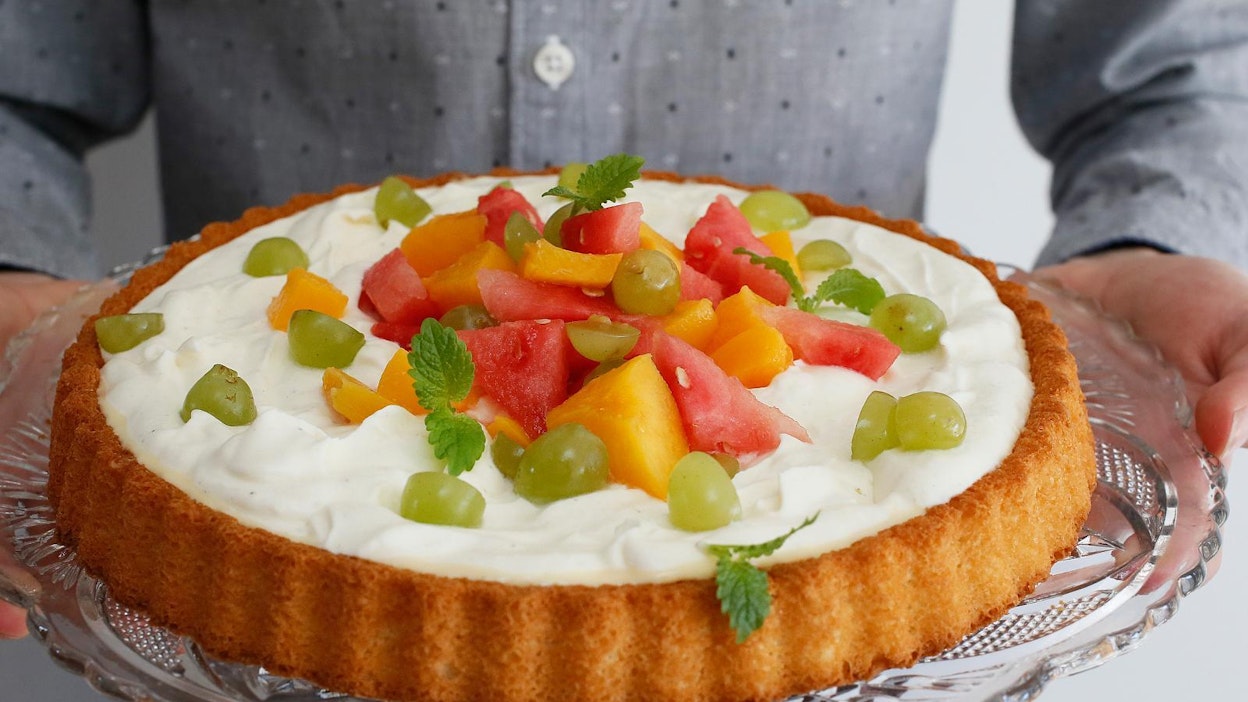 Värikkäillä hedelmillä koristeltu kakku on valmis pöytään kannettavaksi.