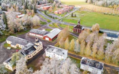 Jokioisten suojeltuja talousrakennuksia dronen ikuistamana: vasemmalla alareunassa talli ja maneesi sekä kivimakasiini ja Impilinna. Keskellä ovat punainen puinen tapulimakasiini ja Työteho, joiden takaa näkyy Luonnonvarakeskuksen keskuskampus.