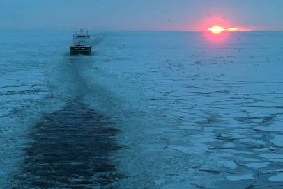 Jäänmurtaja Otso avustaa rahtilaivaliikennettä Perämerellä. Avustettava alus seuraa Otsoa avatulla väylällä auringon noustessa.
ITÄMERI LAIVA MERENKULKU TALVI