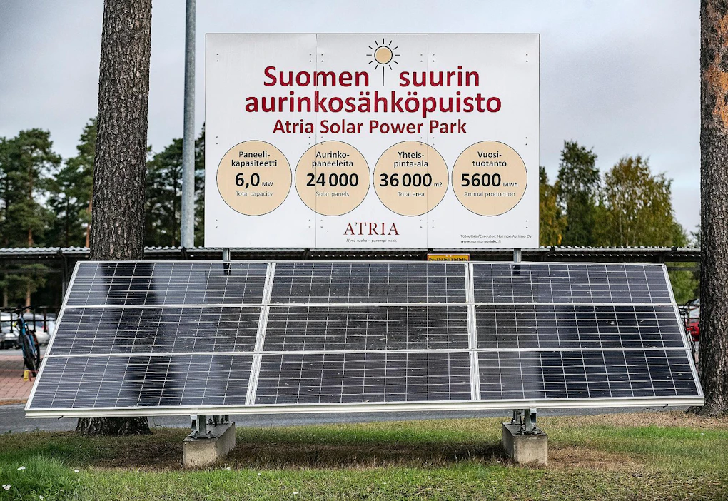 Kuvassa aurinkopuiston info-taulu vuonna 2018. Paneeleita on maassa sekä rakennusten katoilla ja seinillä.