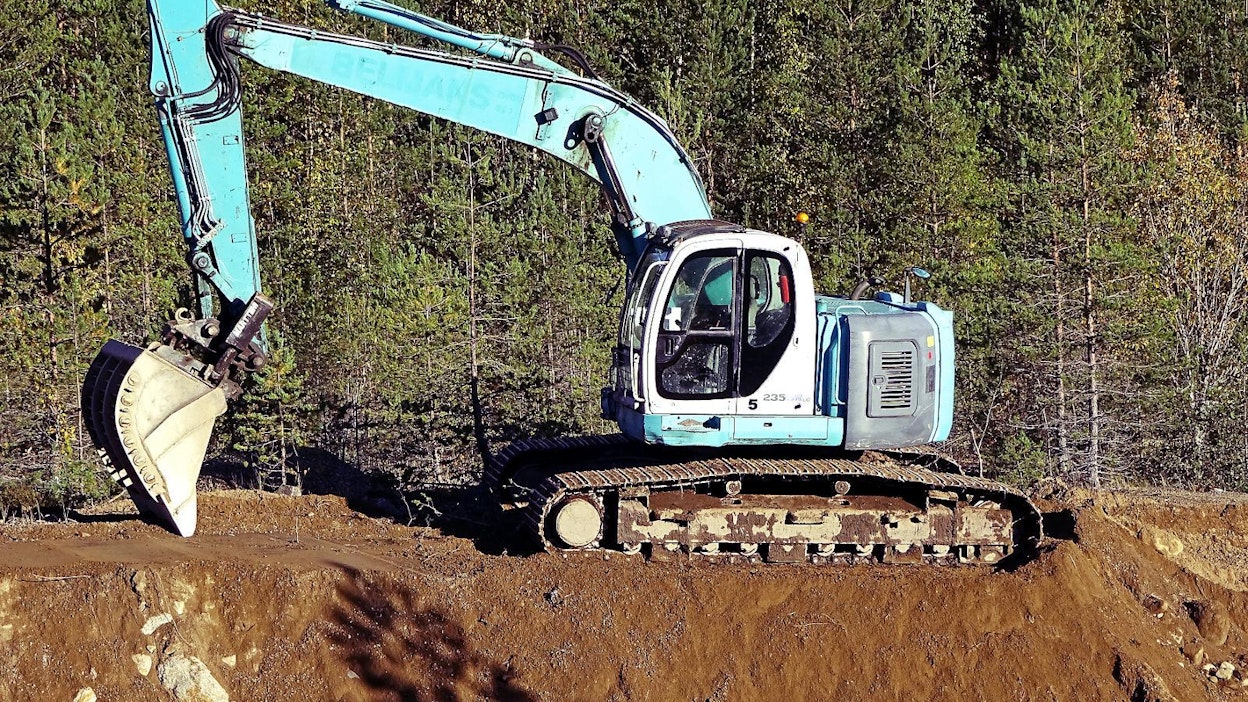 Ensimmäiset Kobelco SK235 SRLC -kaivinkoneet valmistuivat vuoden 2003 aikana. Alkuvaiheessa koneiden kaivupuomit tehtiin päästä päähän 9 mm:n levystä, kuten tässä kuvan kaivinkoneessakin. Melko pian valmistaja muutti rakennetta siten, että puomin alaosa alettiin valmistaa paksummasta levystä. Ratkaisu on nykyisin hyvin yleinen tämän kokoluokan koneissa. Tässä tapauksessa vahvistus tuli tehdyksi jälkikäteen samalla kun puomiin syntynyt vaurio oli joka tapauksessa pakko korjata.