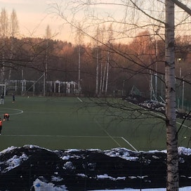 Helsinkiläisen pallokentän laidalla on lumikinoksia, jotka ovat mustuneita tekonurmen rengasrouheesta. Kuva kevättalvelta 2018.