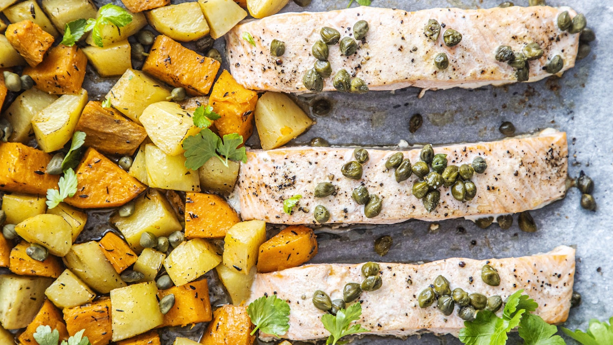 Uunilohi kypsyy perunan ja bataatin rinnalla.