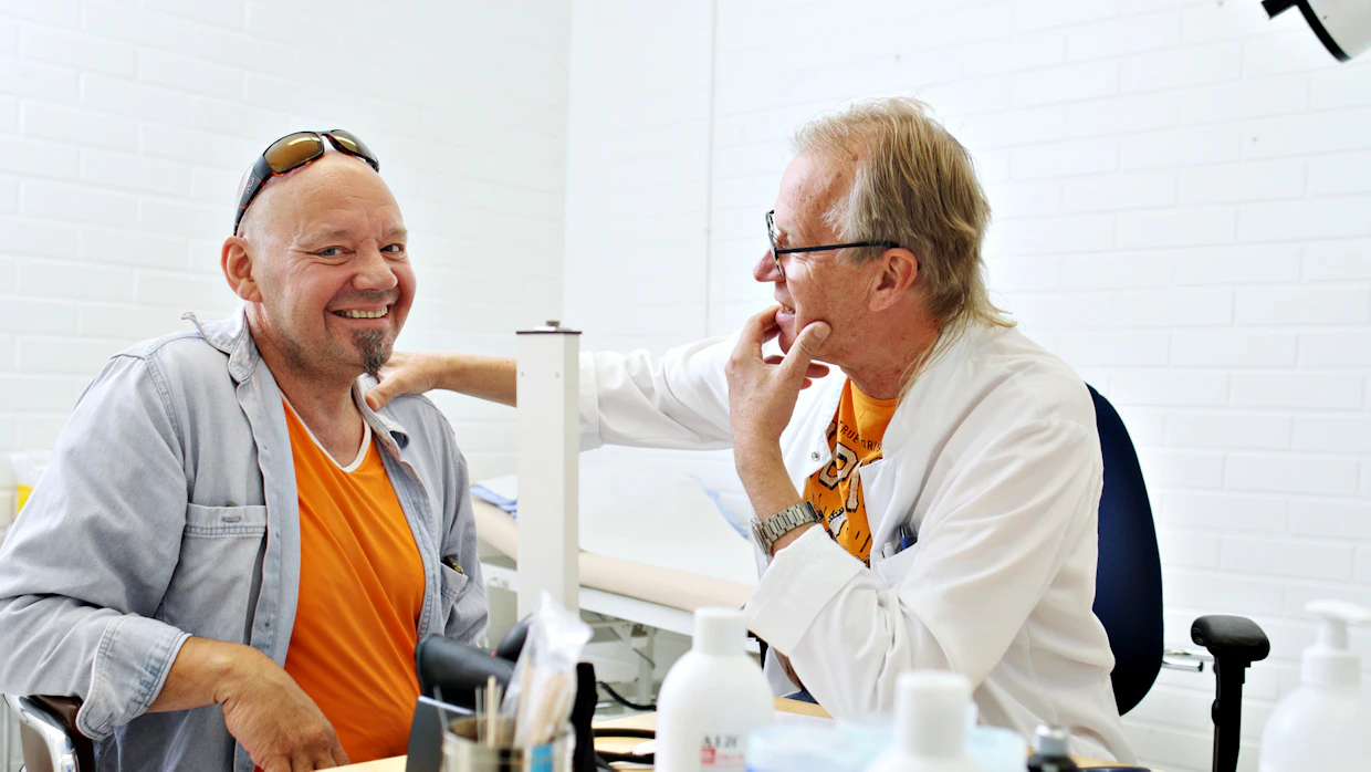 68-vuotias Tapani Kiminkinen on lääkäri, joka koskettaa potilasta. Hän pitää kosketusta merkityksellisenä erityisesti hoivakodeissa oleville mummoille ja papoille. Vastaanotolla viljelijä Hannu Jokinen.