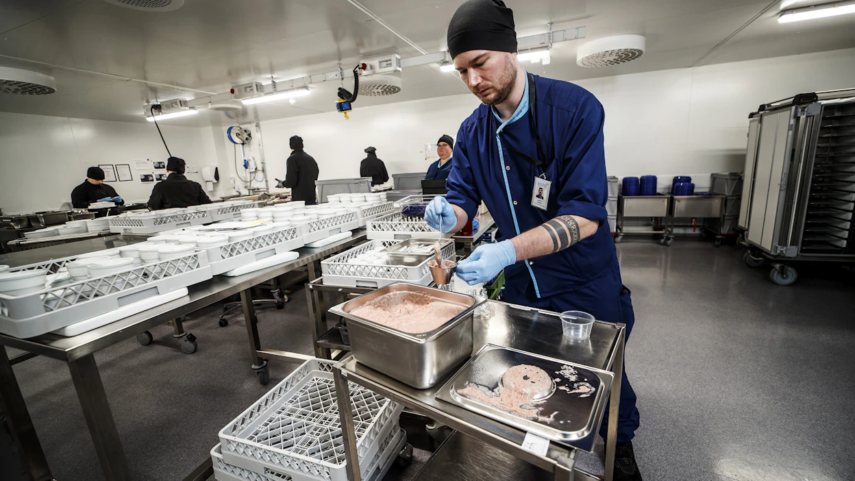 Ruokapalvelutyöntekijä Valtteri Lepistö annostelee vispipuuroa keskitetyn jakelun tilassa. Oikealla on vaunu, johon tarjottimet laitetaan ja joka jäähdytetään nestemäisen hiilidioksidin avulla.