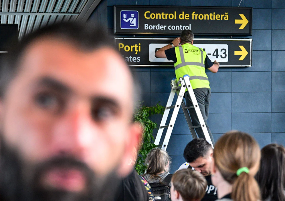 Työntekijä muttuu rajatarkastuksiin ohjaavia kylttejä lentoasemalla Romanian Otopenissa. Lehtikuva/AFP.