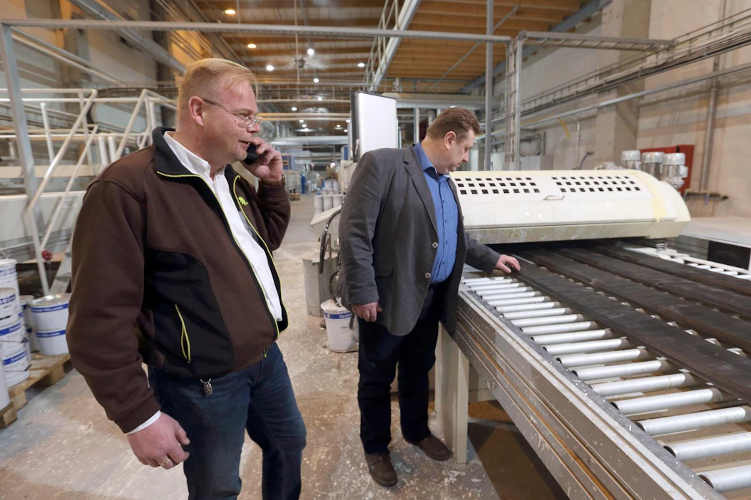 Toimitusjohtaja Markku Heinonen (oikealla) tarkastaa Aureskosken tehtaan pintakäsittelylinjalta valmistuvaa saunapaneelia. Vasemmalla tehdaspäällikkö Simo Arvela.