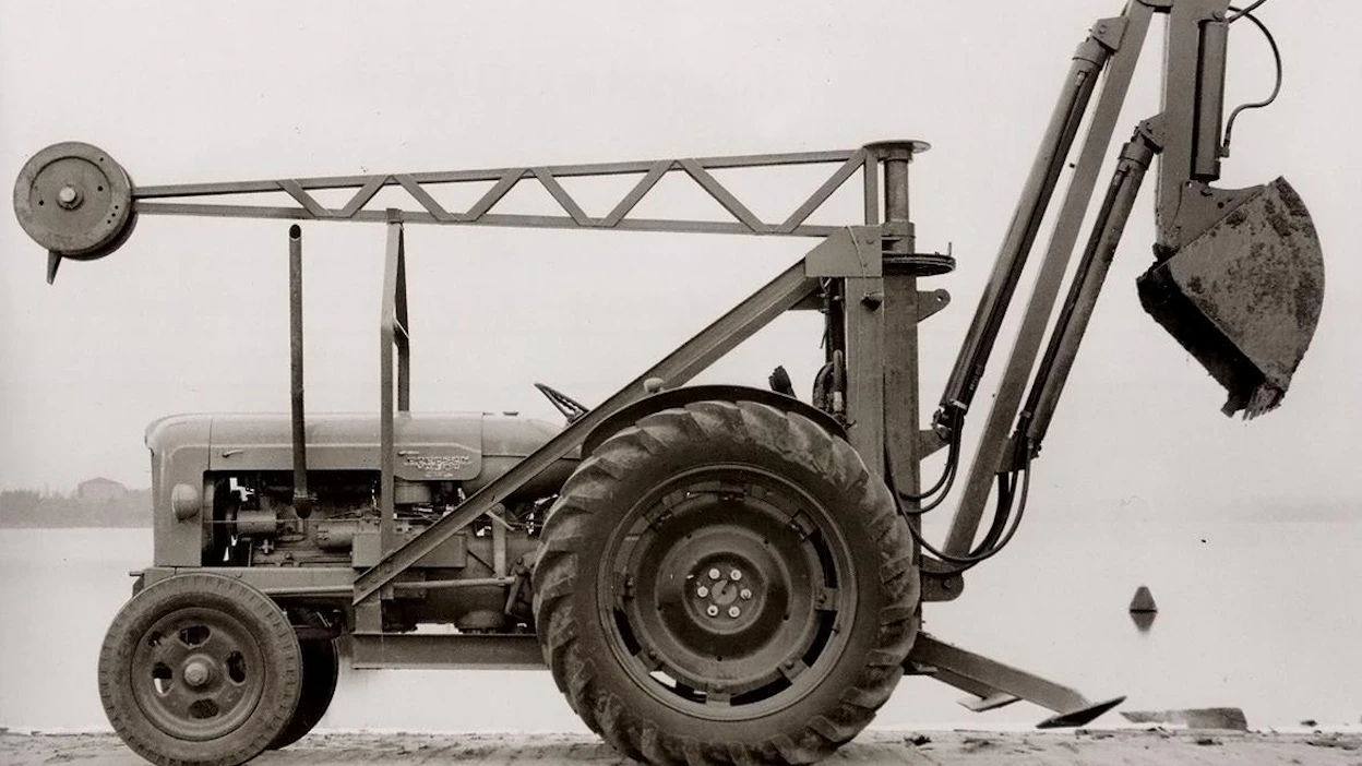 Santahaminan konepajan ensimmäinen kaivinkoneproto kuvattuna konepajaa lähellä sijainneella laiturilla 1954. Tämä kone poikkesi melko tavalla myöhemmistä ja esimerkiksi kaivulaitteen käännön sylinteri oli vielä tässä vaiheessa sijoitettu pystyasentoon kiinni vasempaan takatolppaan. Pian huomattiin, että tarvitaan suurempi sylinteri, jotta kääntövoima riittäisi ja silloin sylinteri sijoitettiin ohjaamon yläpuolelle. Kone edusti aikansa uusinta tekniikkaa ja sen edistyksellisyyttä kuvaa se, että kyseinen kone oli todennäköisesti ensimmäinen Euroopassa valmistettu hydraulinen traktorikaivuri.