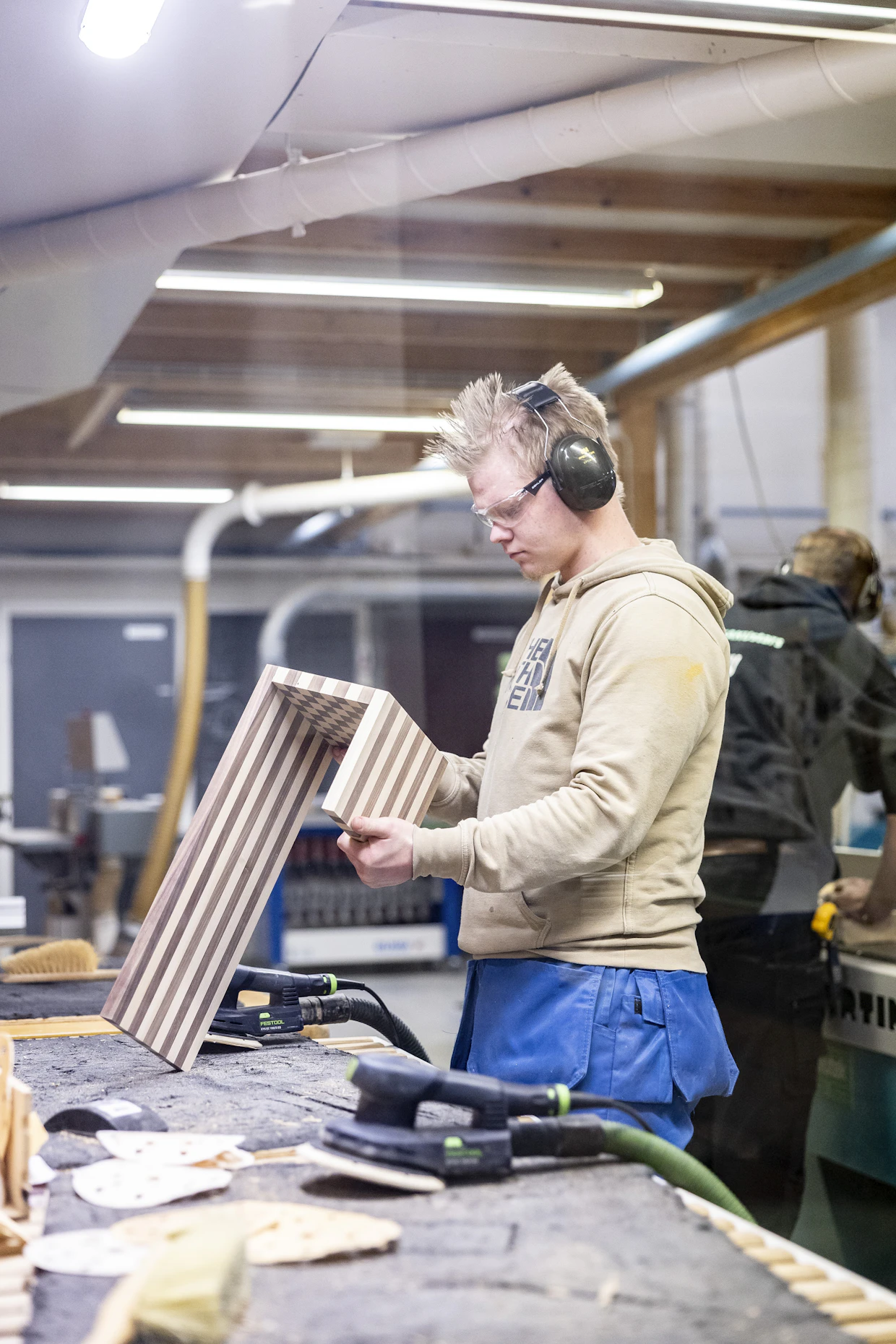Iiro Yrjölä viimeistelee sohvan juomatasoa hiomakoneella.