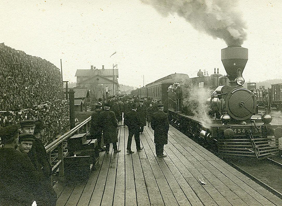 Riihimäen rautatieasema. Aseman edessä laiturilla matkustajia ja raiteella höyryveturi Sk3, nro 434. Kuva on arviolta vuodelta 1907.