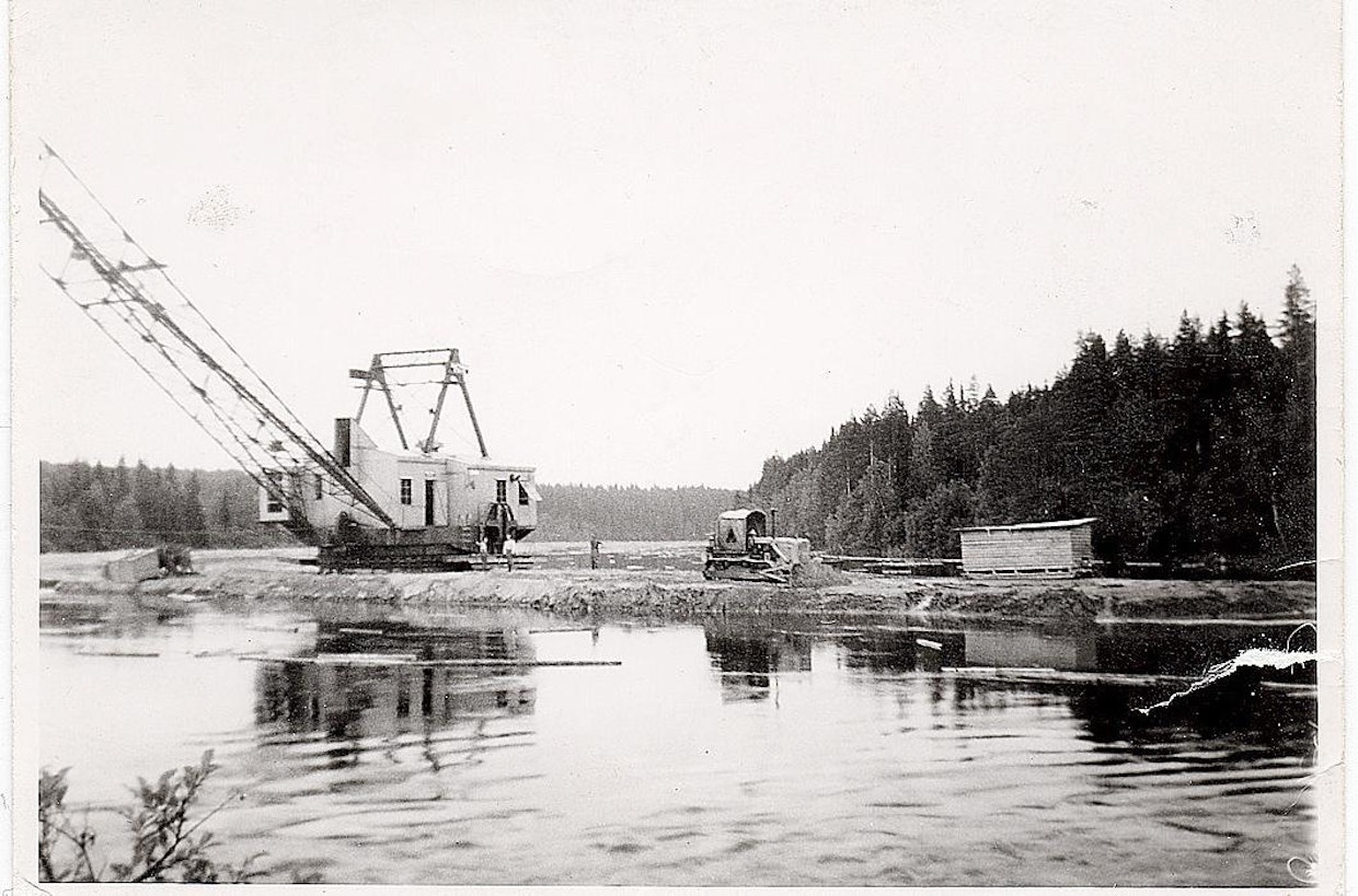 Bucyrus W200 kaivamassa Seitenoikealla vähän ennen Jokikylää. Koneen saamiseksi jokeen riittävän lähelle kaivukohtaa, sillä nostettiin aluksi joen pohjasta soraa, josta muodostettiin puskukoneella tasoittamalla työpenger. Penkereen piti mennä joen yli viistoon. Suoraan se ei voinut mennä, ettei virta tule liian kovaksi ja ala syömään penkkaa. Jokimaa kantoi hyvin, kun virta huuhtoi hienon aineksen pois ja jäljelle jäi karkeaa kiviainesta. Sen sijaan peltomaat eivät tahtoneet kantaa raskasta konetta.