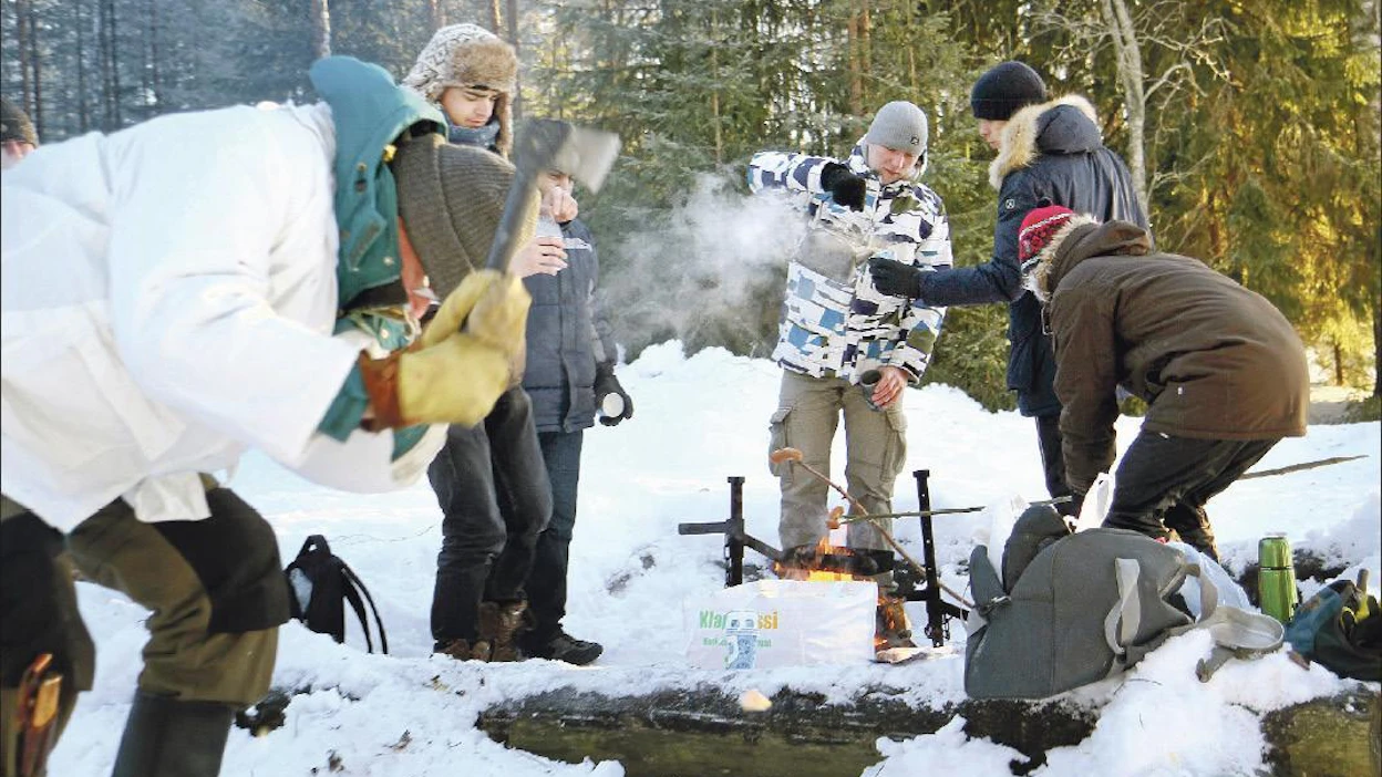 Kansainvälisiä opiskelijoita Itä-Suomen yliopistossa luotsaava amanuenssi Markku Ropo näyttää etualalla, kuinka tervasrosomännystä syntyy sytykettä, taustalla jo lämmitellään nuotiolla. Lari Lievonen