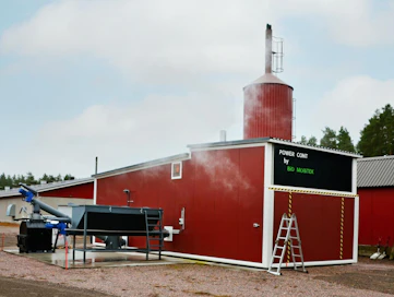 Siisti lämpökontti vanhan lämpölaitoksen vieressä on melko huomaamaton. Uuden laitoksen ominaisuudet parantavat kotieläintilan hygieniaa ja alentavat tuotantokustannuksia. Taustalla näkyy vanhan laitoksen rakenteita.