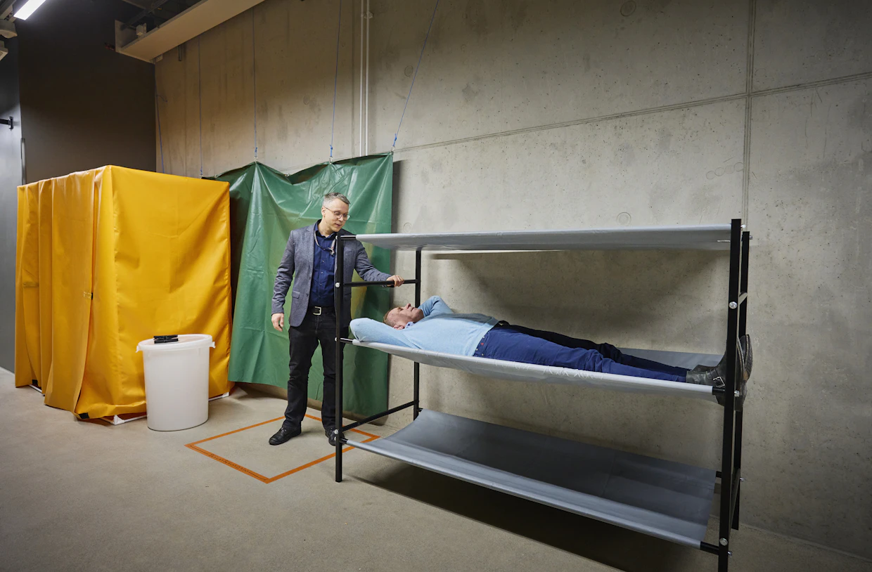 Asko Muhonen testaa kerrossänkyä. Mikko Moilasen takana wc-koppi ja tilanjakajapressuja.