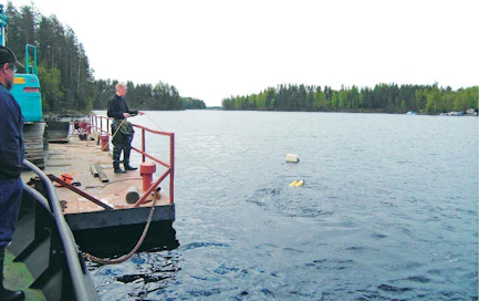 Paikallisen pelastuslaitoksen sukeltaja on menossa kiinnittämään nostoliinaa auton vetokoukkuun. Lautan kannella on toinen sukeltaja pitelemässä varmistusköyttä.