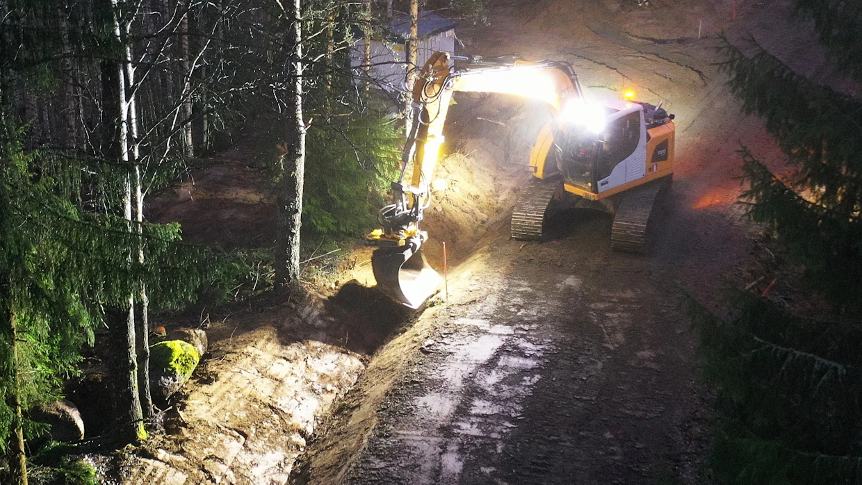 Kun kaapeli on asennettu kaivantoon, perässä tulevalla kaivinkoneella jälki, tässä tapauksessa tienpiennar, muotoillaan laadukkaasti. Pylväsmuuntamoiden sijaan kaapeloinnissa ovat käytössä kaivurin takana näkyvät puistomuuntamot.