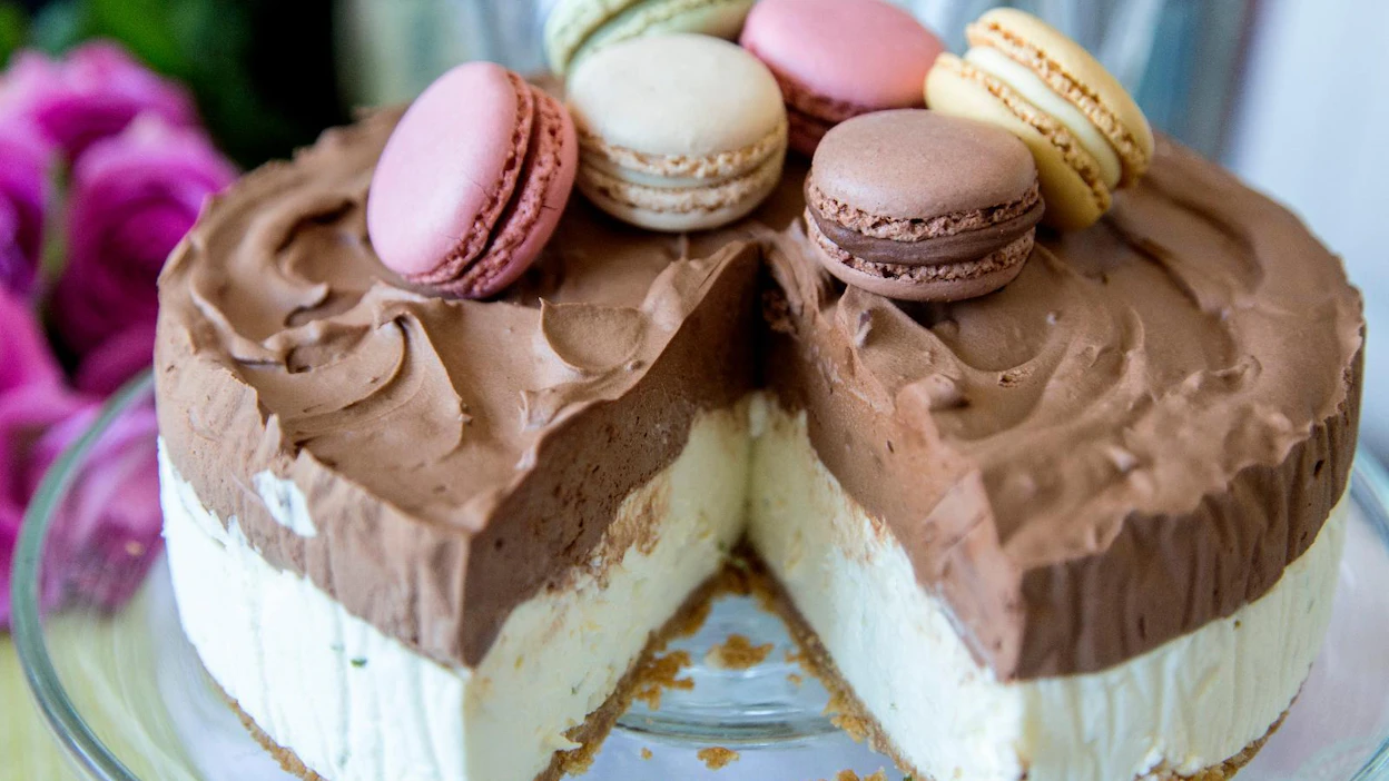 Valkosuklaalla ja tummalla suklaalla maustettu moussekakku valmistuu ilman uunia. Valmiilla macarons-leivoksilla saat kakulle näyttävän ja makoisan koristelun.