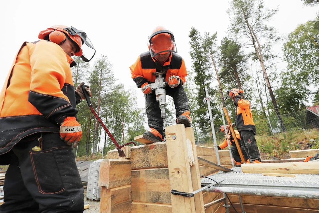 Ammattiopisto Lappian maahanmuuttajataustaiset metsuriopiskelijat veistävät hirsistä saunatupaa. Dar Reh vääntää hirttä kohdalleen ja Lui Chor poraa reikää vaarnatapille.