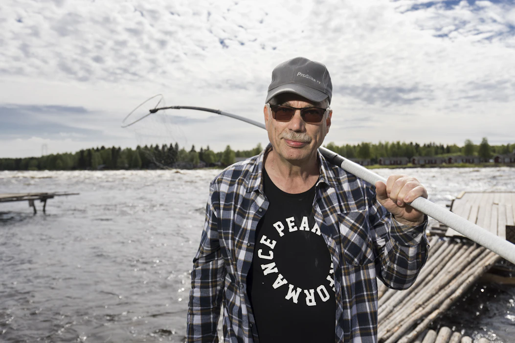 Markku Vaaraniemi pitää olallaan perinteistä lippoa. Taustalla pauhaa Kukkolankoski. Vastarannalla on Ruotsi.