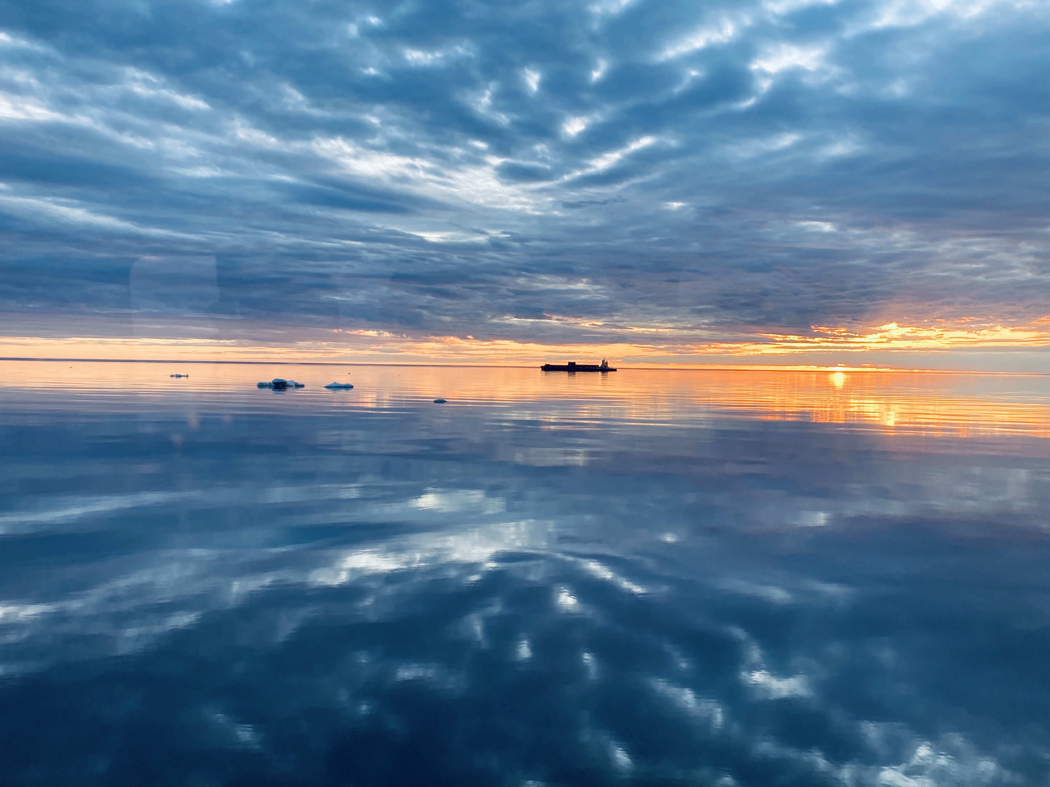 Oranssi väylä. Rahtialus ja irtojäät purjehtivat auringonlaskuun jossakin Perämerellä.