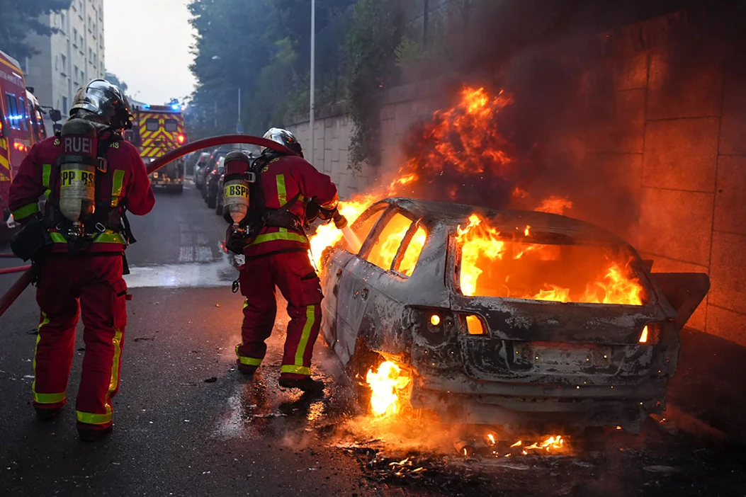 Ampumistapauksen jälkeen Pariisin läntisellä esikaupunkialueella Nanterressa puhkesi mielenosoituksia, joissa muun muassa sytytettiin tuleen roska-astioita. Kuvassa pelastajat sammuttavat palavaa autoa alueella. LEHTIKUVA/AFP.