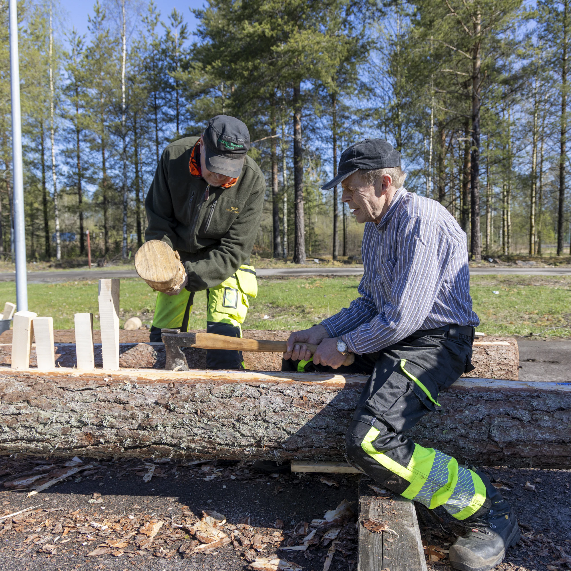 Säröslaudan teko vaatii malttia. Martti Koivumäki näyttää, miten puu halkaistaan kirveen ja puukiilojen avulla. Restauroinnin opiskelija Harri Nieminen käyttää nuijaa.
