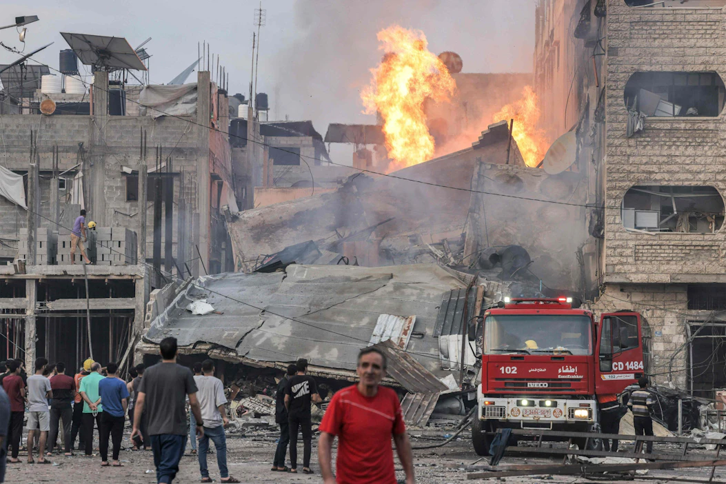 Ihmiset katselivat palavaa ja romahtanutta rakennusta Gazan kaupungissa Israelin pommitusten jälkeen keskiviikkona. LEHTIKUVA/AFP.